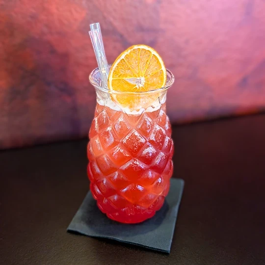 Finished cocktail, served in a pineapple-shaped glass and decorated with a slice of dehydrated orange, highlighting the elegant and colorful presentation of the drinks at Inferno Gastro Bar.